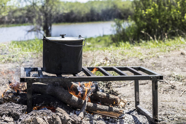 Cooking fish soup in a pot over a fire. Field kitchen. Hike. Camp in the woods. - Photo, image