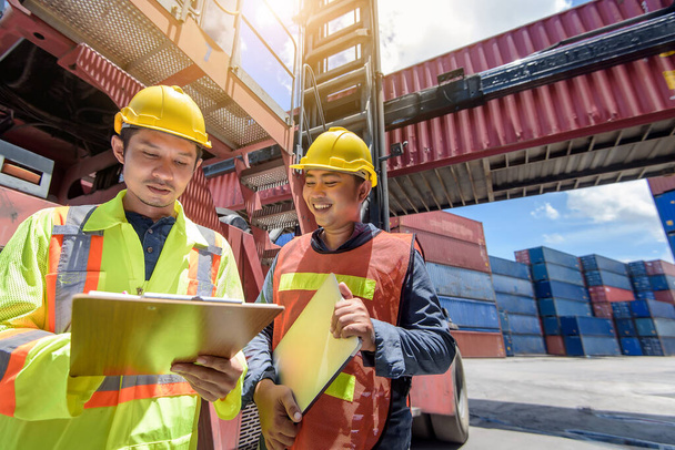 Engineer men wearing yellow hardhat standing near forklift cargo at the container yard and check for control loading Containers box from Cargo freight ship for import and export. Teamwork concept  - Foto, afbeelding