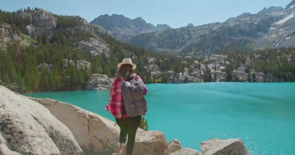 Mujer emocionada por llegar al lago de montaña azul escénico, levanta las manos. 4K - Imágenes, Vídeo