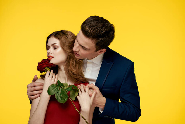 geliefden man en vrouw met een rode roos in hun handen knuffelen op een gele achtergrond romantiek relatie liefde familie - Foto, afbeelding