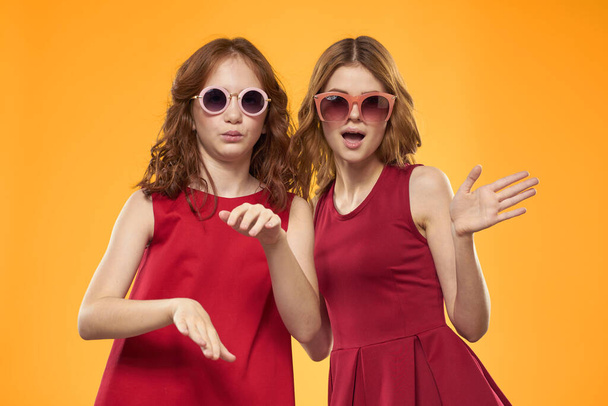 Mujer feliz y niña en vestido rojo se divierten en un fondo amarillo moda emociones hermanas diversión Copiar espacio. - Foto, imagen