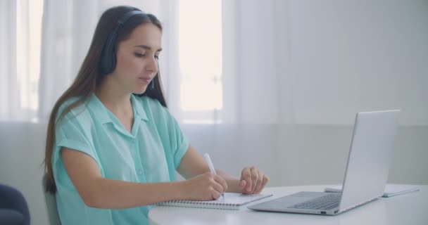 student woman sit at desk at home wear headset talk distantly by video call app and laptop device e-learn language studying with e tutor or classmate do common task remotely, modern tech concept - Πλάνα, βίντεο