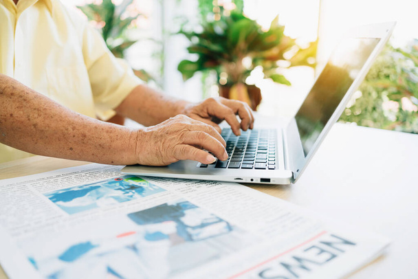 Κοντινό πλάνο ένας ηλικιωμένος συνταξιούχος γέρος χρησιμοποιώντας ένα φορητό υπολογιστή με τα χέρια πατώντας πληκτρολόγιο, ενώ κάθεται στο σπίτι. Χόμπι συνταξιοδότησης και τρόπος ζωής. Ο παππούς εργάζεται από το σπίτι. - Φωτογραφία, εικόνα