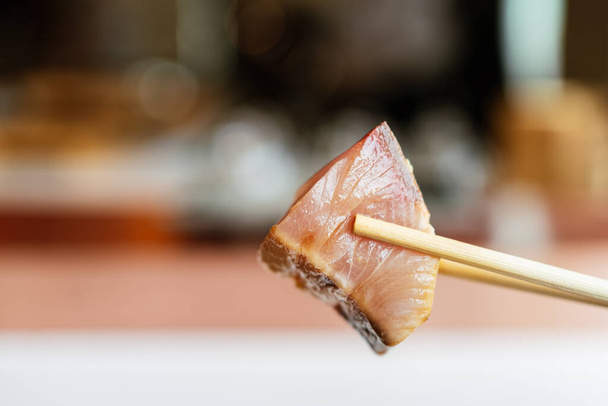 Japanische Omakase-Mahlzeit: geschlossener gereifter Akami-Thunfisch (magerer Thunfisch), der mit Stäbchen kneift. Japanische Luxusmahlzeit. - Foto, Bild