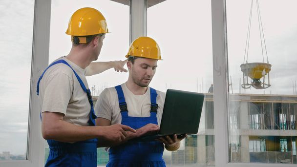 Two builders wearing protective helmets working on a laptop. - Photo, image