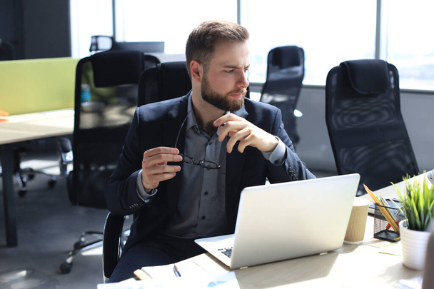 Молодий сучасний бізнесмен працює за допомогою ноутбука, сидячи в офісі
 - Фото, зображення
