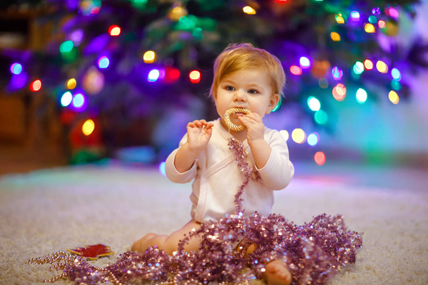 Adorable bébé fille tenant guirlande de lumières colorées dans des mains mignonnes. Petit enfant en vêtements de fête décorant l'arbre de Noël en famille. Première célébration de la fête traditionnelle appelée Weihnachten - Photo, image