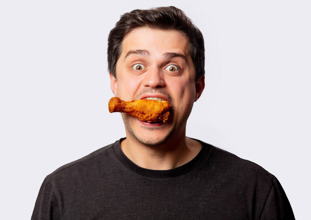 White man in black shirt with chicken drumsticks on white background - Photo, Image