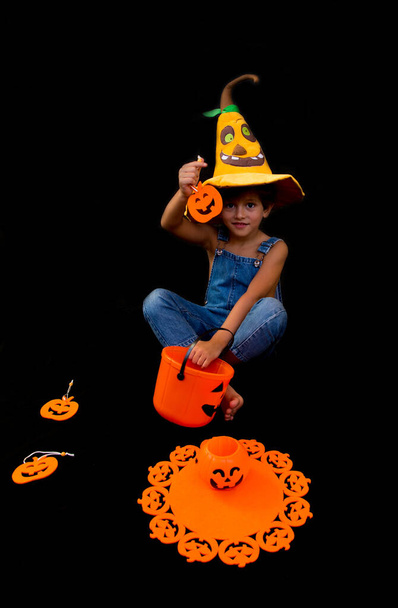Hermoso niño en un fondo negro con un sombrero de calabaza y un cubo en forma de calabaza para pedir truco o tratamiento en la fiesta de Halloween - Foto, imagen