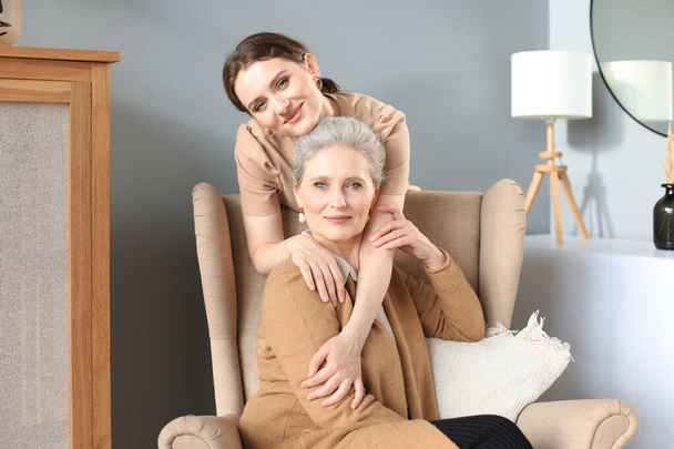 Elderly middle mother sitting in a chair and her daughter are hugging, looking at camera, trusted relations - Фото, изображение