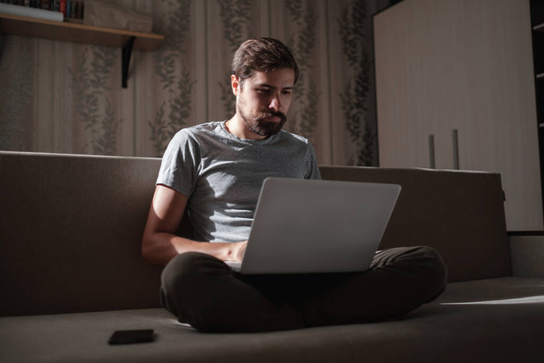 Trabajo remoto. Hombre trabajando en el ordenador portátil sentado en el sofá en casa. Copiar espacio para texto. freelancer hipster trabaja desde casa, estudiando o comunicándose con parejas - Foto, Imagen