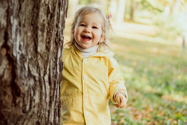 Valkoihoinen lapsi tyttö nauraa kävelee puistossa puun lähellä. - Valokuva, kuva