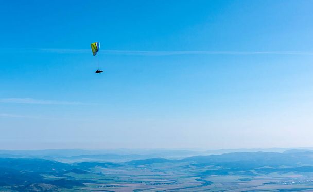 Tatranska Lomnica, Σλοβακία - 15 Σεπτεμβρίου 2020: Αλεξίπτωτο πλαγιάς - Ένα αλεξίπτωτο πλαγιάς που πετά ψηλά πάνω από την κοιλάδα σε μια όμορφη ηλιόλουστη μέρα. - Φωτογραφία, εικόνα
