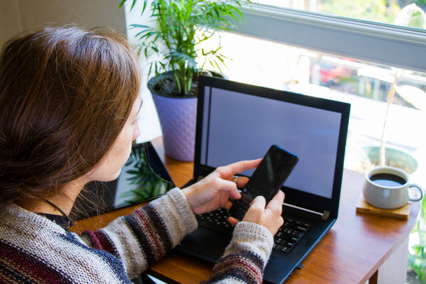 Frau arbeitet mit Notebook am Arbeitsplatz, digitalem Tablet, Mobiltelefon, Kaffee und Pflanzen am Arbeitsplatz, Heimarbeit - Foto, Bild