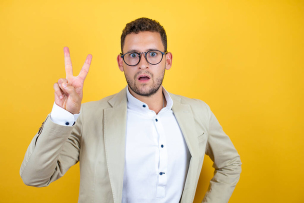 Young handsome businessman wearing suit over isolated yellow background showing and pointing up with fingers number two while smiling confident and happy - Photo, Image
