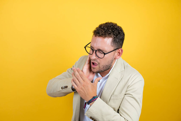 Young handsome businessman wearing suit over isolated yellow background touching mouth with hand with painful expression because of toothache or dental illness on teeth - Photo, Image