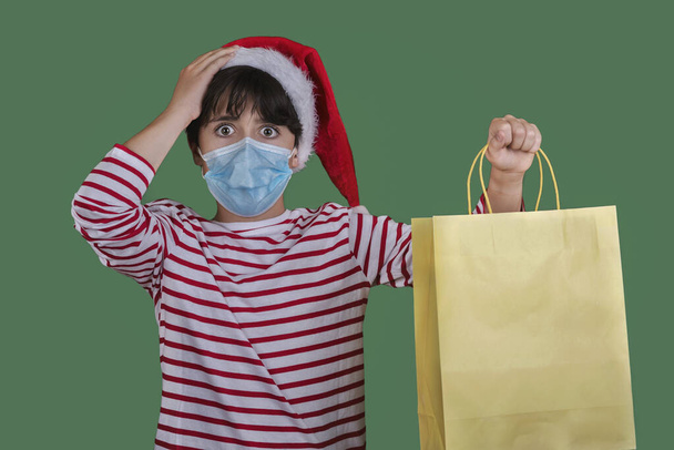 Mutlu Noeller, tıbbi maskeli komik çocuk yeşil arka planda bir alışveriş çantası tutuyor. - Fotoğraf, Görsel