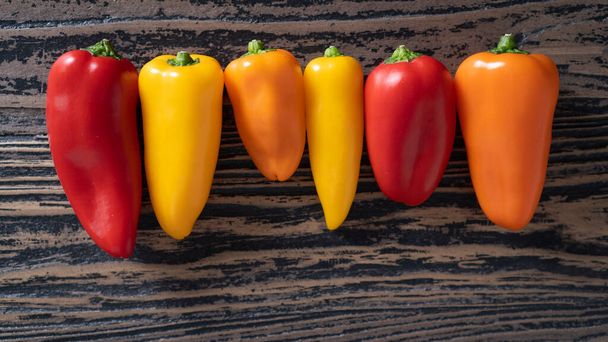 different types of peppers on a wooden table. Bright fresh red, orange and yellow peppers on dark wooden table - Fotoğraf, Görsel