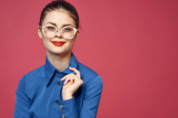 Retrato de uma mulher em óculos e em uma camisa azul lábios vermelhos modelo de fundo rosa - Foto, Imagem