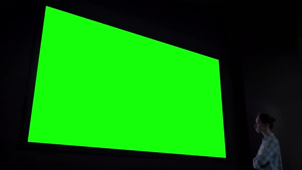 Woman looking at large blank green screen in dark room - chroma key concept - Footage, Video
