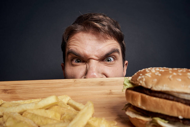 uomo emotivo con pallet di legno fast food hamburger patatine fritte mangiare cibo stile di vita sfondo scuro - Foto, immagini