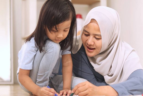 Asian muslim mother drawing with her daughter, single mom teaching baby girl, learning on the floor, happy family concept   - Photo, image