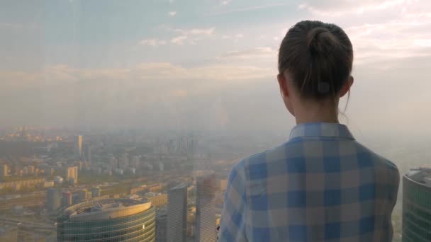 Vista trasera de la mujer mirando espectacular paisaje urbano a través de la ventana del rascacielos - Metraje, vídeo