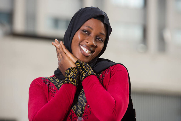 nuori musliminainen seisoo ulkona katsomassa kameraa nauraen kädet yhdessä. - Valokuva, kuva