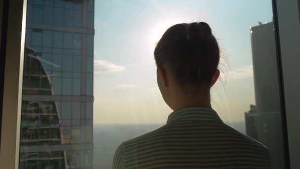 Πίσω όψη γυναικείας σιλουέτας που κοιτάζει το αστικό τοπίο μέσα από το παράθυρο του ουρανοξύστη - Πλάνα, βίντεο