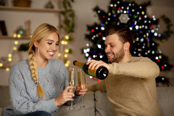 Young couple drinking champagne, celebrating New Year together at home - 写真・画像