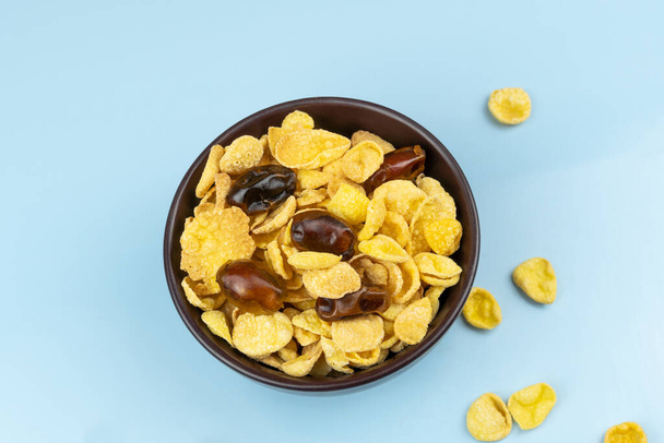 Fiocchi di mais alimentari sani in piatto da vicino con date su sfondo blu - Foto, immagini