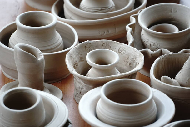 陶芸家の工房のテーブルの上にある手作りの支えのない食器や鍋。セラミック窯で焼成する前の粘土 - 写真・画像