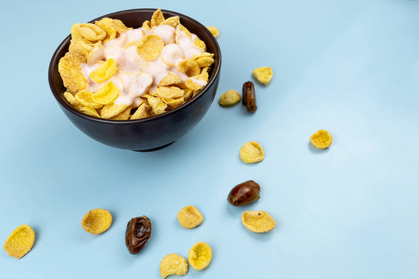 Gesundes Essen Cornflakes in einem Teller mit Joghurt Nahaufnahme mit Datteln auf blauem Hintergrund - Foto, Bild