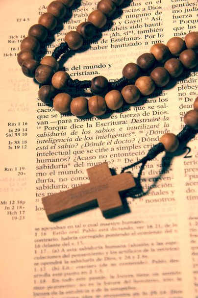Rosario de cruz y cuentas de madera sobre biblia abierta en pasaje en Castellano - Foto, Imagen