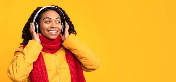 Mujer africana escuchando música en auriculares sobre fondo amarillo - Foto, imagen