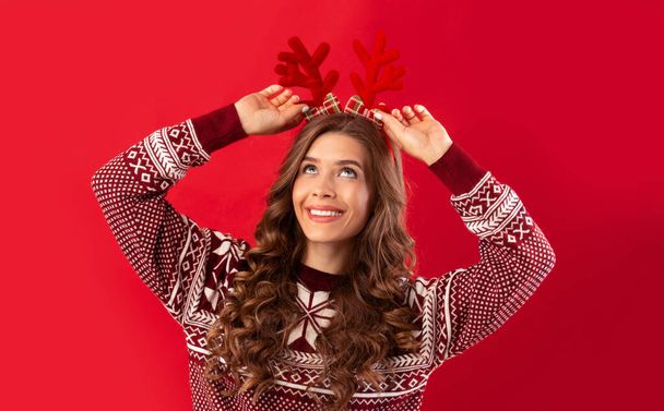 Nyt on joulu. Kaunis nuori nainen villapaita yllään peura sarvet punainen studio tausta, panoraama - Valokuva, kuva