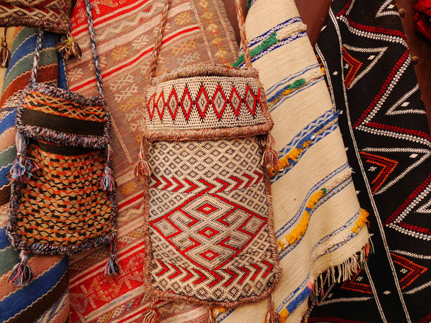 Selección de bolsos y mantas de tela marroquí hechos a mano en patrones tradicionales brillantes y colores vivos, algunos con borlas - Foto, Imagen