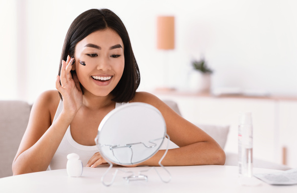 Retrato de mujer asiática limpiando su cara con exfoliante - Foto, imagen