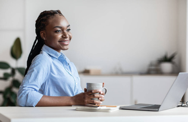 オフィスの職場でコーヒーブレイクを持つ夢のような若い黒人ビジネス女性 - 写真・画像