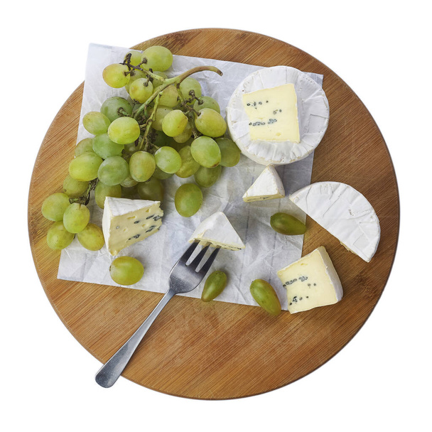 Brie-juuston ja rypäleiden asetelma valkoisella pohjalla eristetyllä puulevyllä. Yläkuva. - Valokuva, kuva