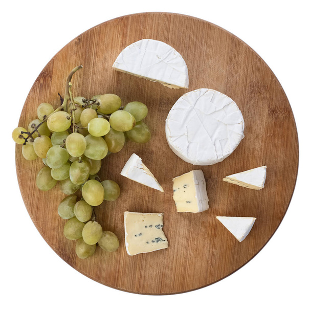 Ainda vida de queijo de brie e uvas em uma tábua de madeira isolada em um contexto branco. Vista superior. - Foto, Imagem
