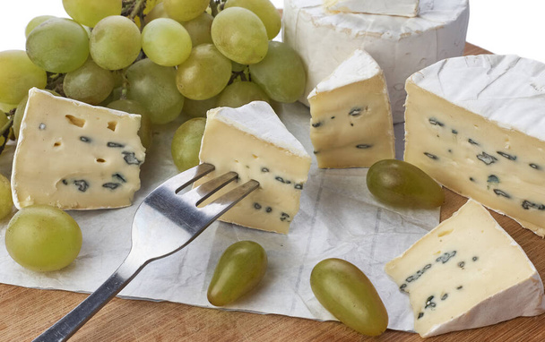 Натюрморт сыра бри и винограда на деревянной доске, изолированной на белом фоне. - Фото, изображение