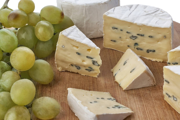 Stillleben von Brie-Käse und Trauben auf einem Holzbrett, isoliert auf weißem Hintergrund. Ansicht von oben. - Foto, Bild