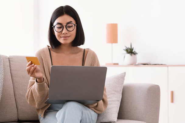 Asian woman making purchases sitting with pc on couch - Photo, Image