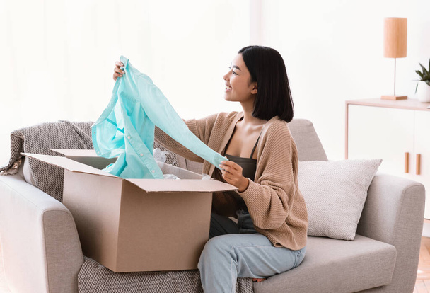 Happy asian buyer unpacking clothes after online shopping - Fotoğraf, Görsel
