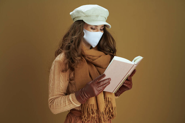 Hello autumn. stylish middle aged housewife in sweater with white medical mask reading book on brown background. - Fotó, kép