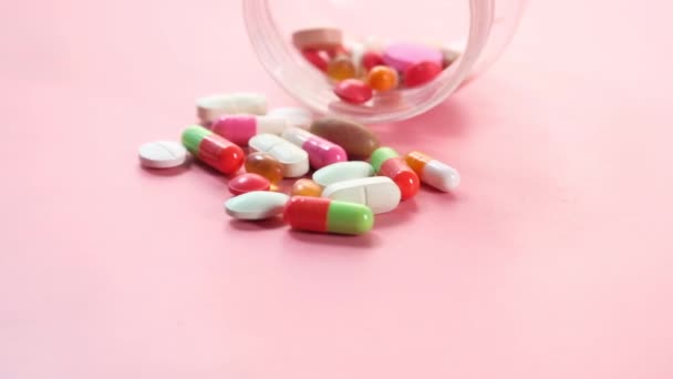 Primer plano de muchas píldoras y cápsulas de colores que se derraman sobre el fondo rosa  - Metraje, vídeo