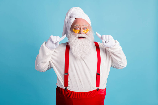 Photo of retired old fat man grey beard direct finger face correcting patches under eye bags wear santa x-mas costume towel turban suspender sunglass isolated blue color background - 写真・画像