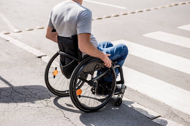Handicapped man in wheelchair preparing to cross the road on pedestrian crossing - Photo, image