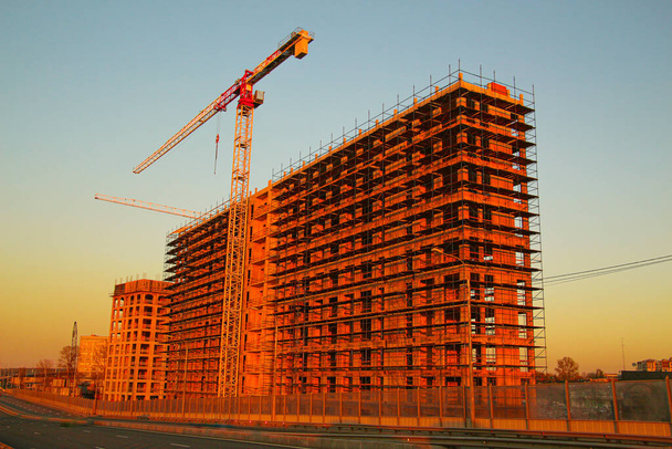 Frame of a multi-storey residential building with high-rise tower cranes illuminated by the rays of the setting sun - Photo, Image